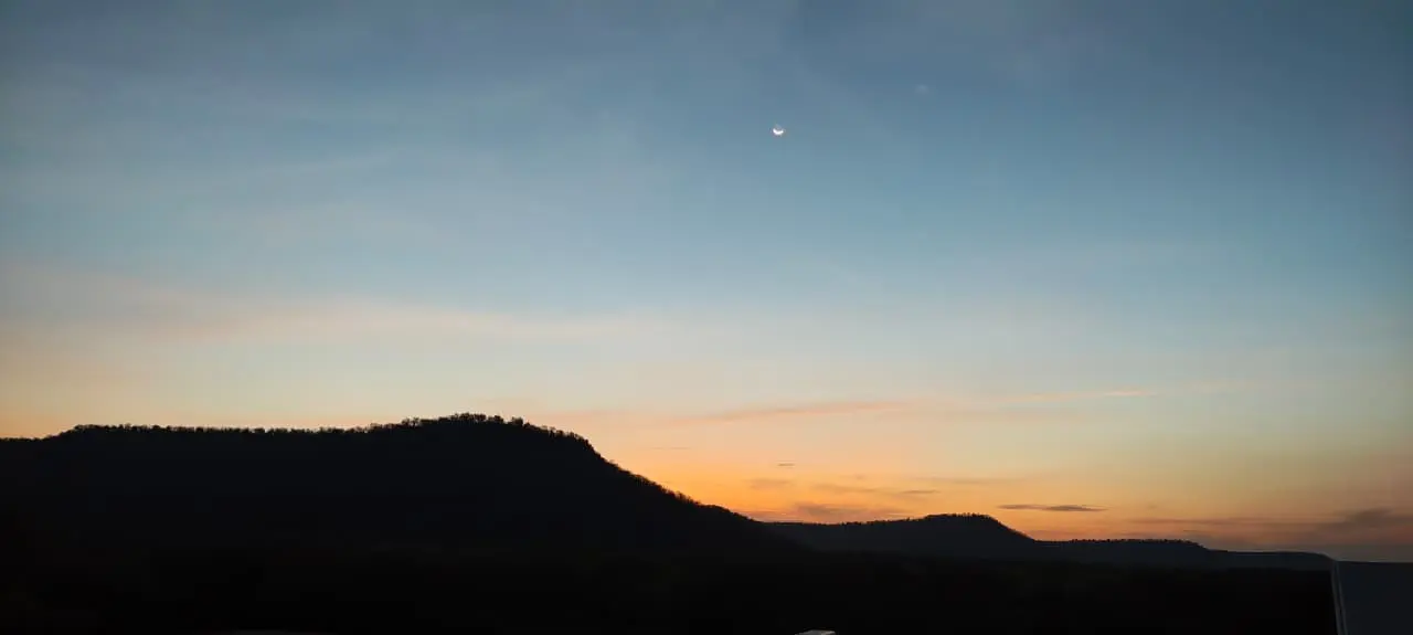 A crescent moon above the forested Shahbad landscape at sunset